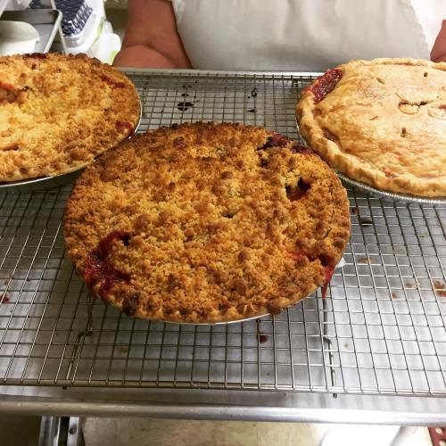 Three freshly baked pies cooling on a wire rack, featuring a crumb topping and a classic pie crust.