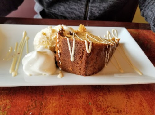 A slice of cake drizzled with icing, served with two scoops of ice cream on a white plate.