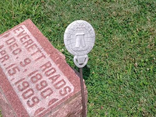 A gravestone with the name "Everett Roads" and dates "Dec. 9, 1890 - Apr. 15, 1909," alongside a decorative metal marker.