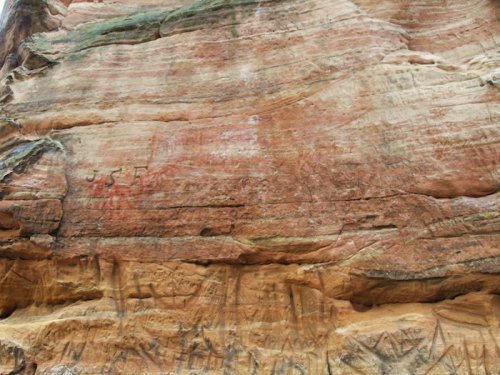 Ancient rock art featuring carvings and red markings on a textured stone surface.