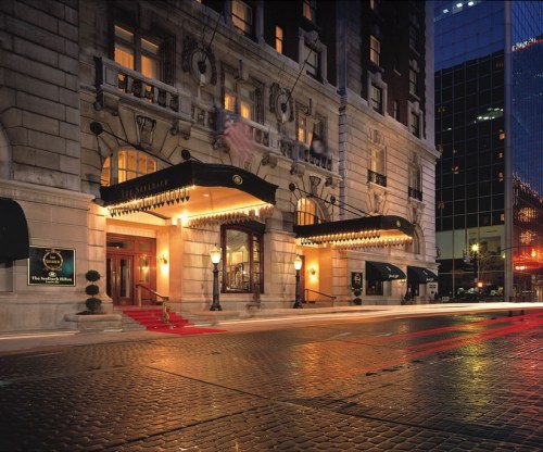 Elegant hotel entrance with red carpet, awnings, and decorative lights, set against a city skyline at night.