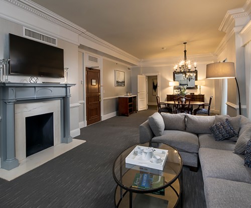 A stylish living room featuring a gray sofa, coffee table, TV, and dining area with a chandelier.