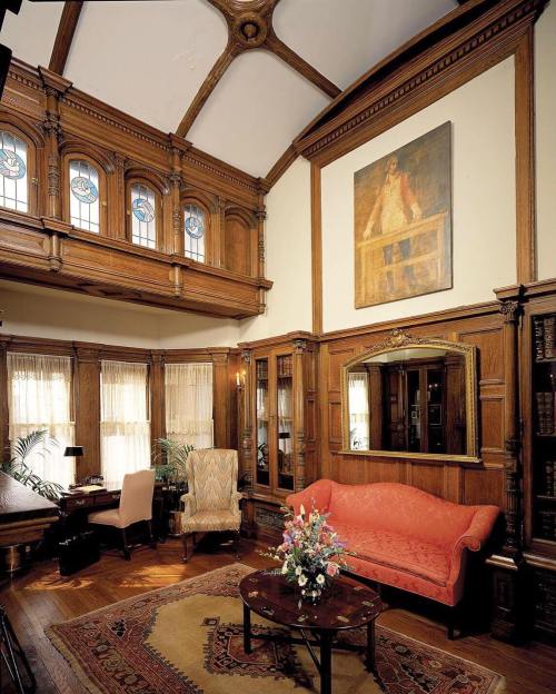 A cozy, elegant room with wooden paneling, a vintage sofa, a large painting, and stained glass windows.