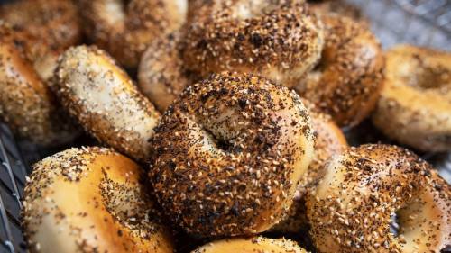 A close-up of a variety of bagels topped with seeds and spices, arranged in a basket.