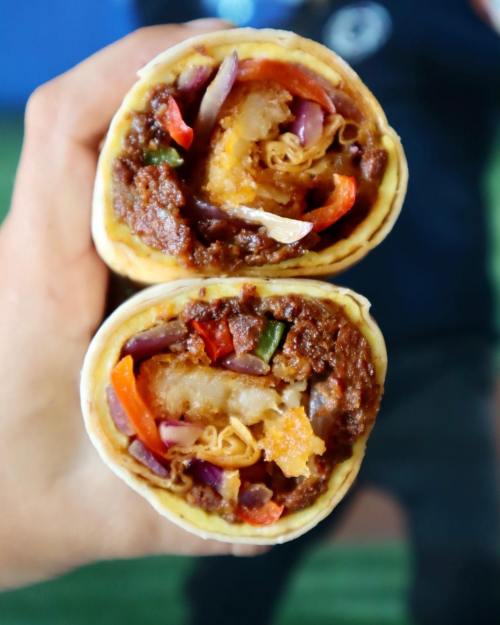 A close-up of a hand holding a halved wrap filled with colorful vegetables and a savory meat mixture.