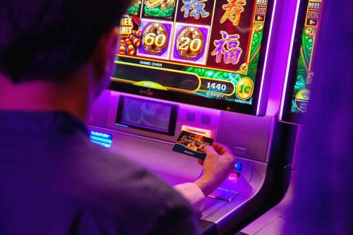 A person inserting a card into a colorful slot machine with a "Game Over" message displayed on the screen.