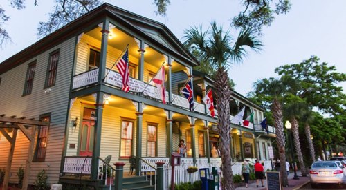 Historic building with colorful flags, palm trees, and warm lighting, set in a lively street scene at dusk.