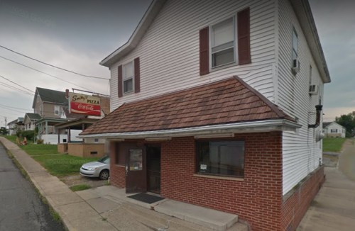 A small, two-story building with a brick facade and a shingled roof, featuring a pizza sign and a parked car nearby.
