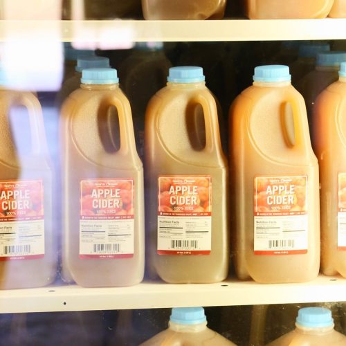 Bottles of apple cider lined up on a shelf, each with a label reading "Apple Cider 100% Juice."