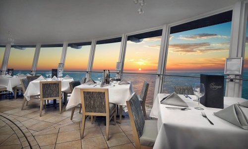 Elegant restaurant interior with white tablecloths, overlooking a sunset view through large windows.