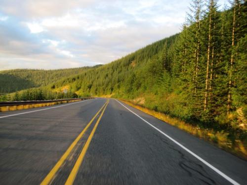 A winding road through lush green hills and trees under a partly cloudy sky.