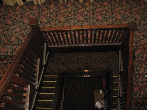 A view from above of a wooden staircase with a floral carpet and a small table at the bottom.