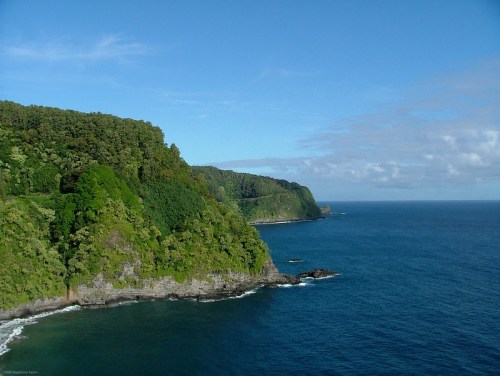 Lush green cliffs meet a calm blue ocean under a clear sky, creating a serene coastal landscape.