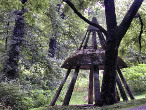 A wooden structure with a dome-shaped roof surrounded by lush green trees in a serene forest setting.