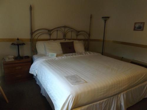 A cozy bedroom featuring a large bed with white linens, a bedside table, lamp, and a simple decor.