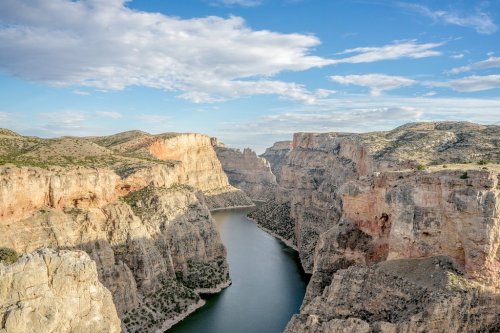 A scenic view of a winding river surrounded by steep, rocky cliffs under a blue sky with scattered clouds.