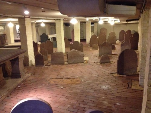 A dimly lit basement with numerous old gravestones arranged on a brick floor.