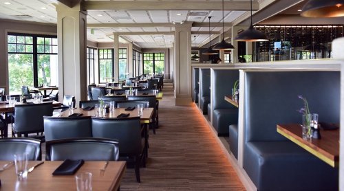 Modern restaurant interior with wooden tables, leather chairs, and large windows, creating a bright and inviting atmosphere.