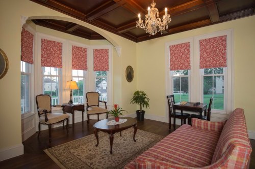 Cozy living room with a striped sofa, chandelier, and large windows adorned with floral curtains. A small table and chairs are present.