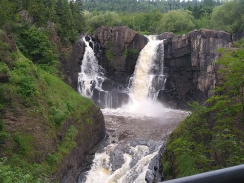 A scenic view of a waterfall cascading over rocky cliffs, surrounded by lush greenery and a river below.