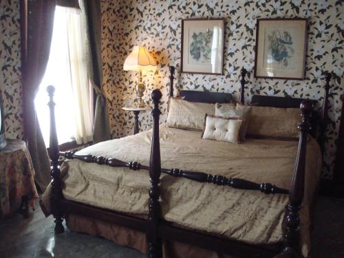 A cozy bedroom featuring a large bed with a gold cover, floral wallpaper, and a lamp beside a window.
