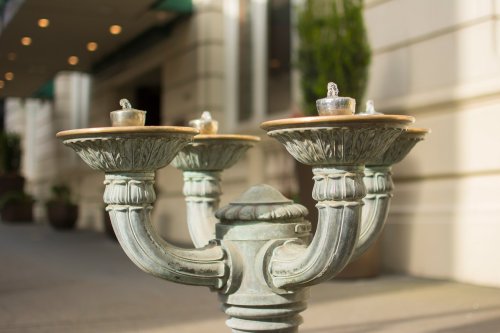 A decorative vintage water fountain with three spouts, set against a blurred background of a building entrance.