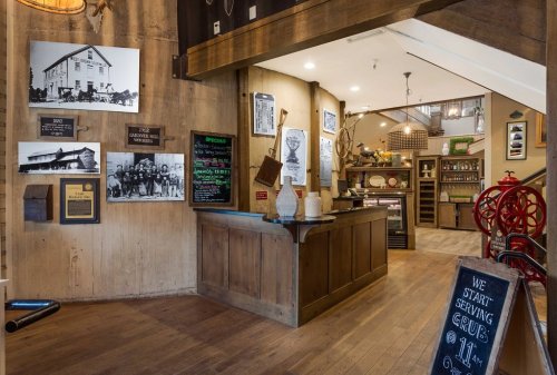 Interior of a rustic café with wooden decor, historical photos on the walls, and a chalkboard sign for service hours.