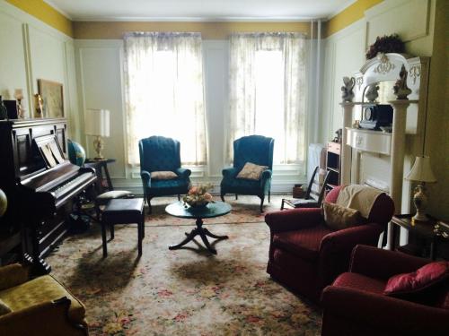 A cozy living room with vintage furniture, a piano, and large windows letting in natural light.