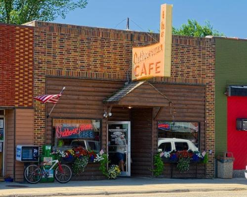 A charming café with a wooden exterior, colorful flower displays, and a vintage sign reading "Outdoor Man Café."