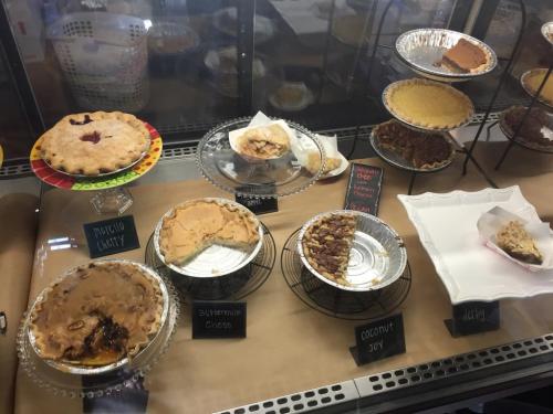 A display case filled with various pies, including cherry, buttermilk, coconut, and pecan, on decorative stands.