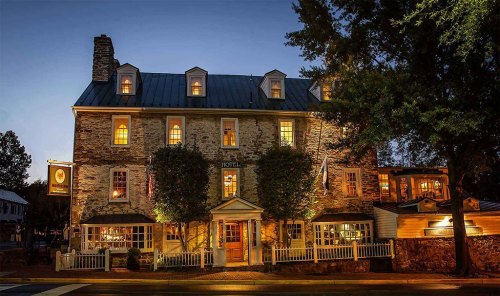Historic stone hotel illuminated at dusk, featuring large windows and a welcoming entrance surrounded by trees.