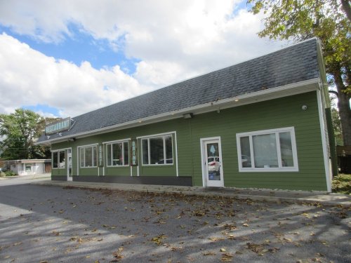 A green restaurant building with large windows, set against a cloudy sky and surrounded by trees.