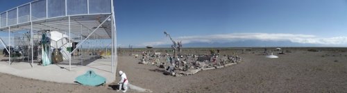 A panoramic view of a barren landscape featuring a structure, sculptures, and a UFO-like object.