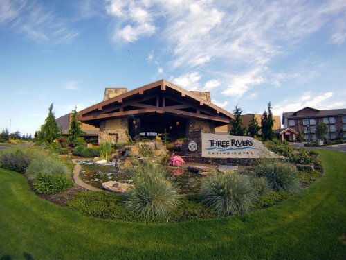 Exterior view of Three Rivers Casino & Hotel, featuring landscaped gardens and a water feature under a blue sky.