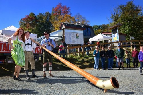 A man and woman in traditional attire pose with a large horn at an outdoor festival, with a crowd in the background.