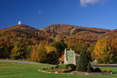 A scenic view of Sugar Mountain with vibrant autumn foliage and a ski resort in the background under a clear blue sky.