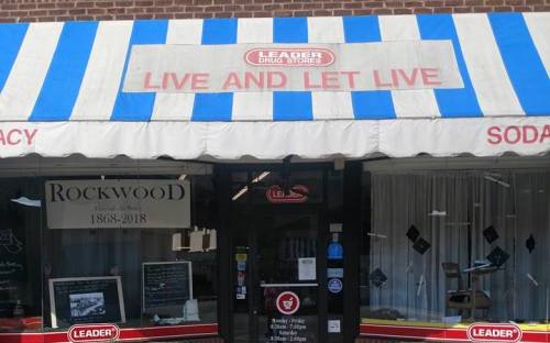 A storefront with a striped awning reading "LIVE AND LET LIVE" and "LEADER DRUG STORES," featuring a display window.