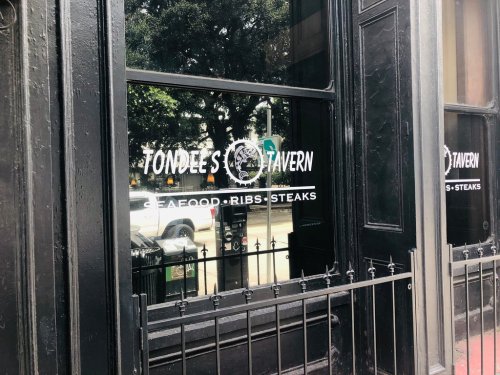 Window of Tondé's Tavern featuring a sign that reads "Seafood, Ribs, Steaks" with a view of the street outside.