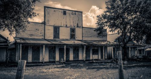 A weathered, abandoned building with a rusty roof and boarded windows, set against a cloudy sky.