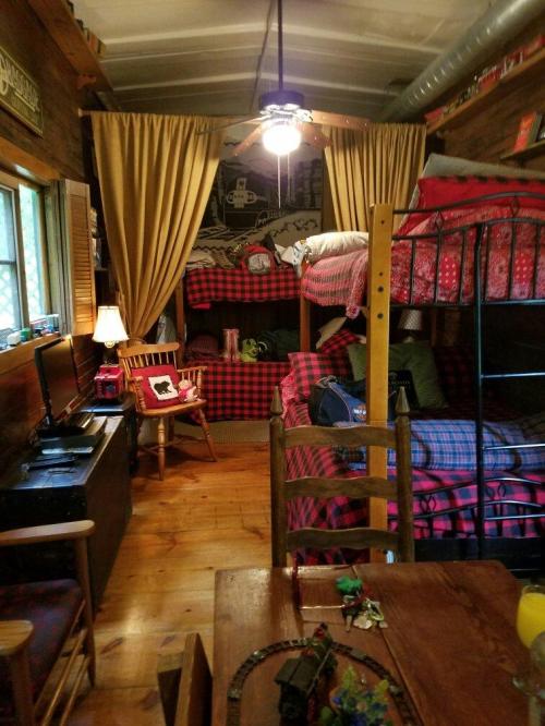 Cozy cabin interior with bunk beds, plaid decor, wooden furniture, and warm lighting.