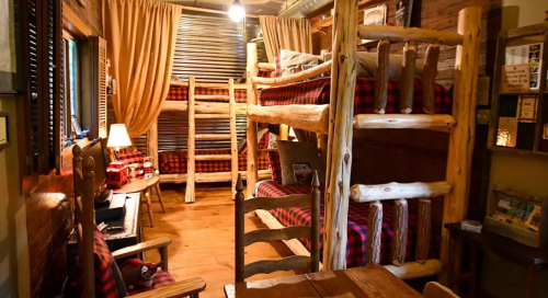 Cozy cabin interior with wooden bunk beds, plaid bedding, and warm lighting, creating a rustic atmosphere.