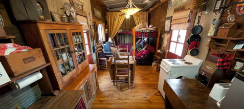 Cozy rustic interior featuring a bedroom, dining area, and kitchen with wooden furniture and warm decor.