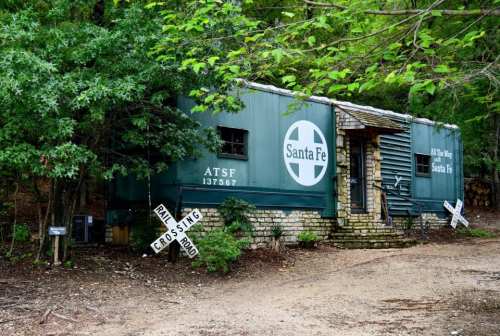 A green train car converted into a building, surrounded by trees and a gravel path, with a Santa Fe logo on the side.