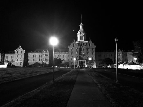 Historic building illuminated at night, featuring a clock tower and surrounding grassy area.