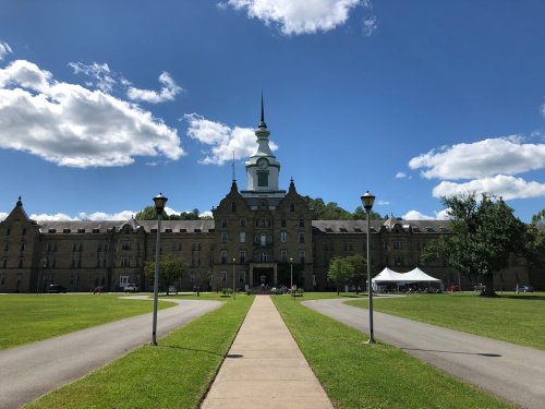Historic stone building with a clock tower, surrounded by green grass and blue skies with fluffy clouds.