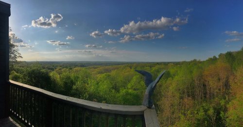 A panoramic view of lush green hills under a blue sky with scattered clouds, seen from a wooden balcony.