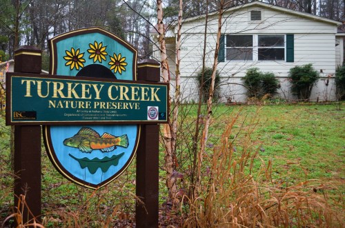 Sign for Turkey Creek Nature Preserve in front of a house, surrounded by greenery and trees.