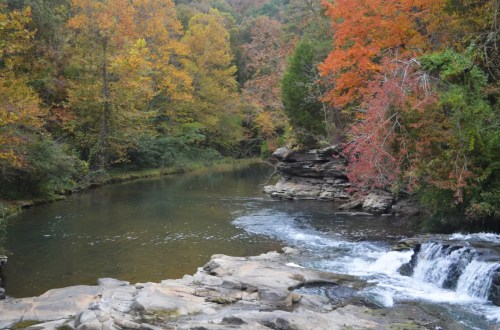 A serene river flows through a forest with vibrant autumn foliage in shades of orange, red, and yellow.