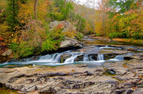 A serene waterfall cascades over rocky terrain, surrounded by vibrant autumn foliage and lush greenery.