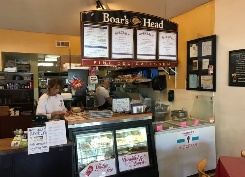 A deli counter with a menu board, staff serving food, and a display case for ice cream and desserts.
